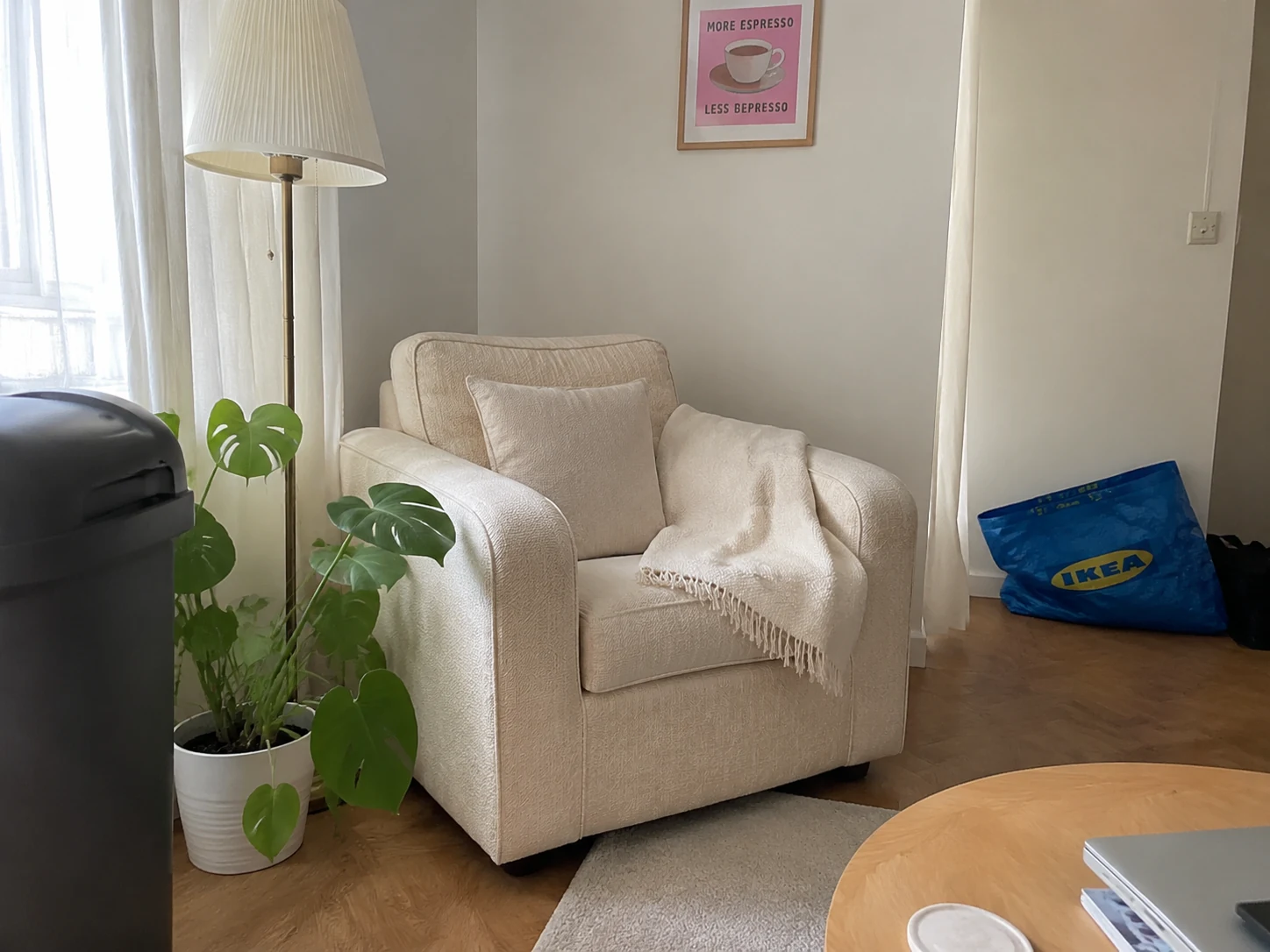 Styled living room corner with cream armchair and plant, a rubbish bin at the left edge and a crumpled IKEA bag on the floor in the background