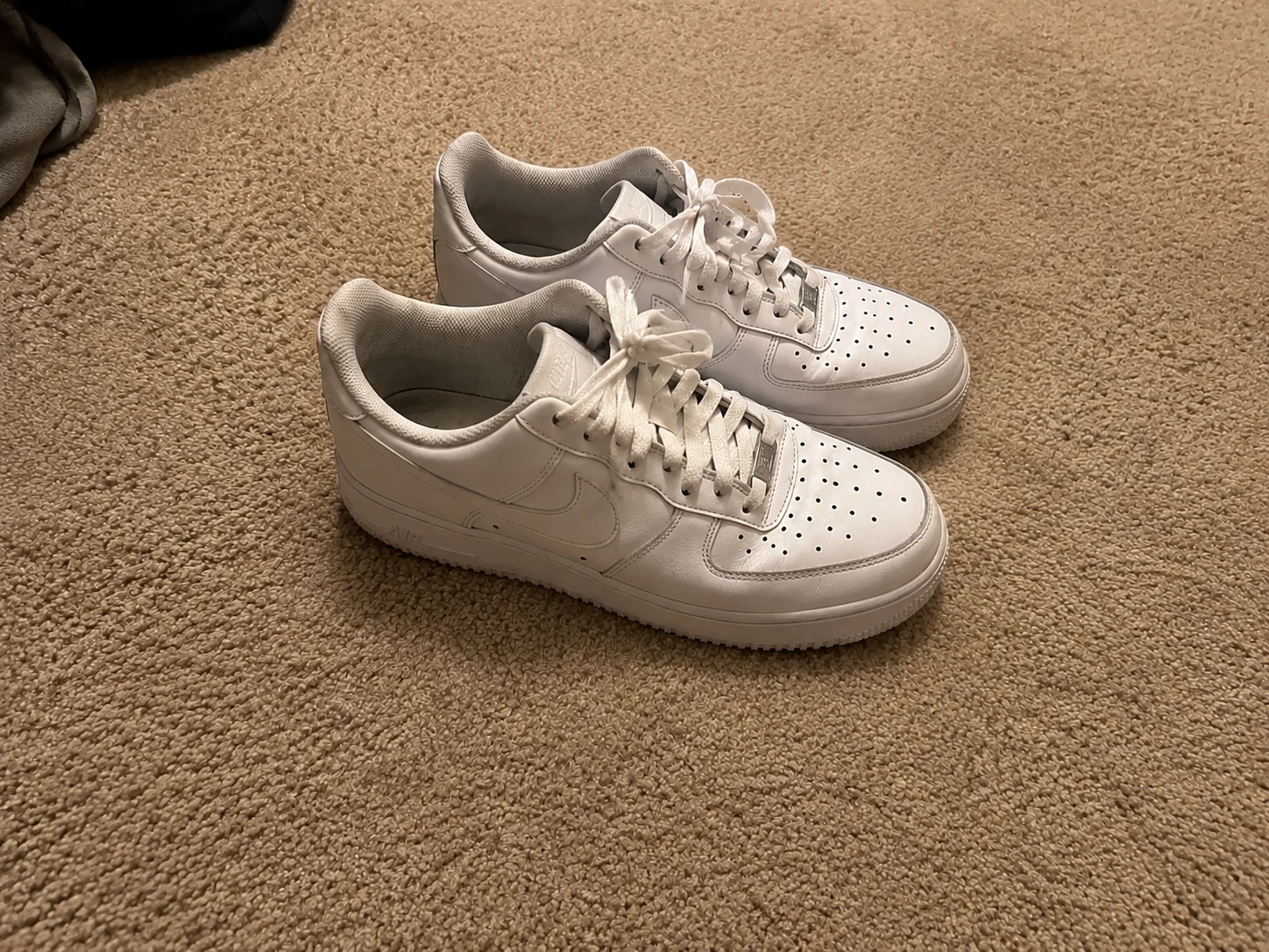 White Nike Air Force 1 sneakers on carpet with foot, cable, and water bottle removed for a clean marketplace listing photo