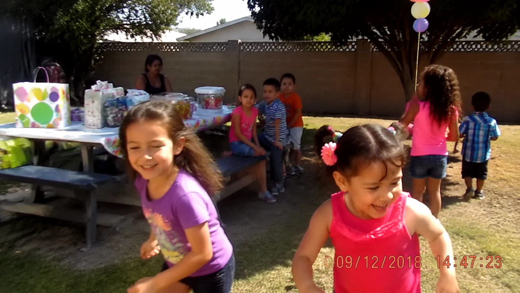 Home video footage of children playing outdoors with an orange camcorder date-time stamp in the bottom-right corner