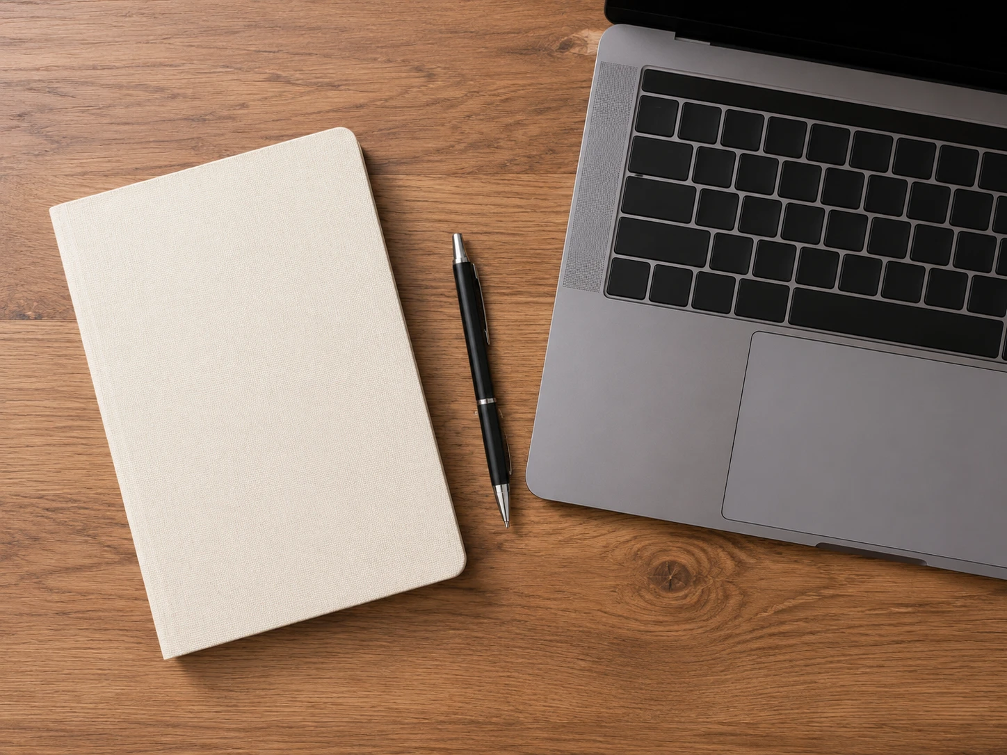Top-down flat lay of a notebook, pen, and laptop keyboard on a wooden desk